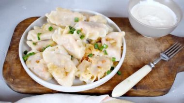 Homemade dumplings, vareniki, varenyky, pyrohy with stewed cabbage sprinkled with onion on plate.Traditional ukrainian popular national dish,cuisine served with sour cream on gray background.
