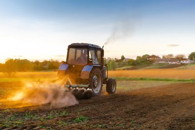 Günbatımında ilkbaharda çiftlikte tarım tarlası süren modern mavi traktör makineleri. Çiftçi tarım yapıyor, ekin, ekin, kırsal alanlardan önce toprak ekiyor..