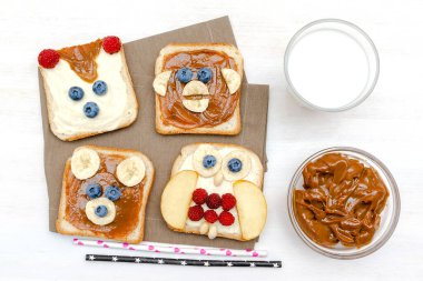 Komik şirin ayı, maymun, tilki, baykuş suratlı sandviç fıstık ezmeli tost ekmeği, muz, yabanmersini, ahududu, süt. Çocuklar bebeğin tatlı, sağlıklı kahvaltı, öğle yemeği sanatı, yakın plan, üst manzara.