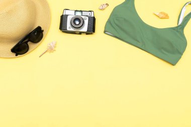 Travel vacation summer flat lay, accessories objects, hat, sunglasses, clothes, bathing suit, camera, seashells on yellow background with copy space, planning trip adventure.