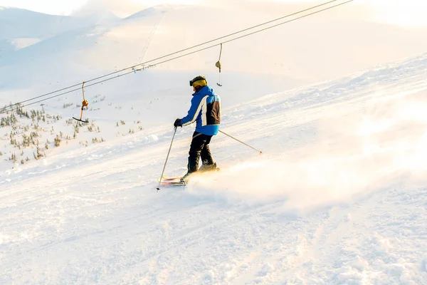 Man in winter overalls skiing on fresh powder snow hill at high Carpathian mountains in sunset light at winter alpine ski resort holiday,outdoor nature landscape, Ukraine, Europe.extreme sport.
