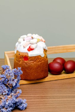Paskalya bayramı yemekleri konsepti. Beyaz kremalı ev yapımı Paskalya pastası, jöle şekeri, tatlı pudra, renkli yumurtalarla süslenmiş, ahşap arka planda çiçek açan fotokopi alanı. Seçici odak.