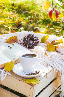 Bir fincan kahve, latte, çikolatalı tatlı çörek, krema, kitap, sıcak içecekler, parkta sıcak ekoseli açık hava, güneşli yaz günlerinde elma bahçesi..