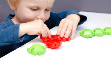 Mozaik yapımcısıyla oynayan küçük bir çocuk. Bebek, plastik blokların figürlerini yapıyor. Çocuk mantığı, motor becerileri gelişimi, anaokulu. Erken duyusal eğitim..