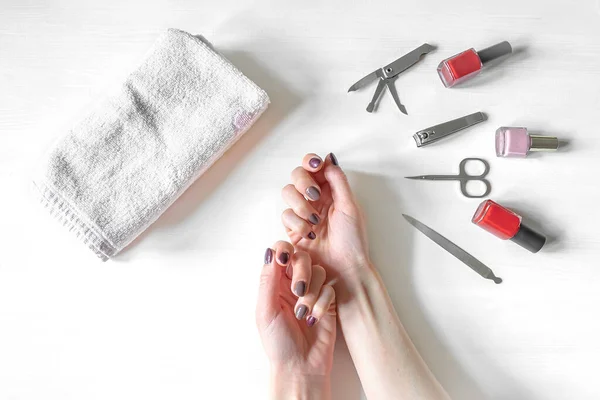 Closeup of hands with polished nails and manicure instruments, bottles of nail polish. caucasian woman receiving french manicure at home or at nail salon. selfcare, beauty procedures yourself.
