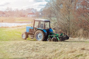 Mavi, küçük, modern traktör makineleri güneşli bir günde çiftlikte tarla sürerler. Çiftçi bitki ve ekin ekmeden önce toprak ekip biçiyor ve ekiyor, kırsal doğa manzarası..