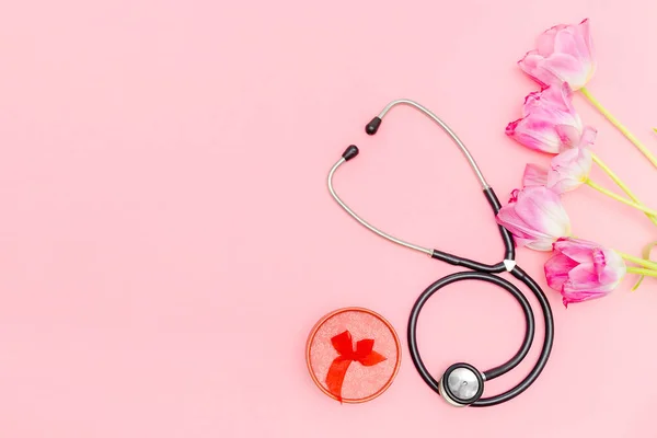 National Doctors or nurse day greeting card with stethoscope, bunch of tulips flowers and present box on pink background.Health medicine Day.Copy space for text.mockup.