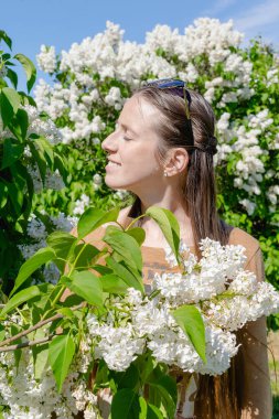 Beautiful thoughtful happy young girl woman surrounded by blooming white flowers in lilac garden. Enjoying the smell of lilac in spring in sunny day.incredibly floral. Nature, bokeh effect. beauty.