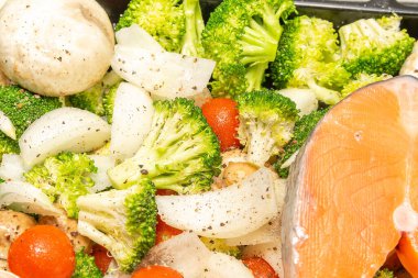 Raw fresh cut salmon fish steak slices on cherry tomatoes,champignons mushrooms,broccoli vegetables, organic sea bass preparing for cooking,baking in stove.vegetarian vegan healthy diet food.