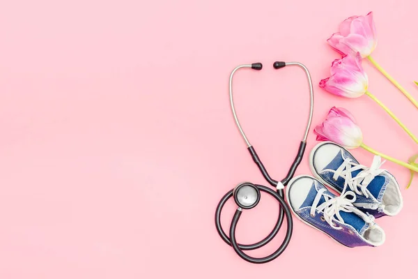 National Doctors or nurse day greeting card with stethoscope, bunch of tulips flowers,babys childs sneakers shoes on pink background.Health medicine Day.Pregnancy,motherhood, obstetrics,pediatrics.