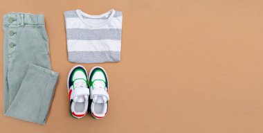 Bebek ayakkabısı, gömlek ve kot pantolon. Bahar, sonbahar ya da yaz için çocuk kıyafetleri ve aksesuarlar. Moda çocuk kıyafetleri, bej kahverengi arka planda giysiler. Düz yatıyordu, üstten, yukarıdan..