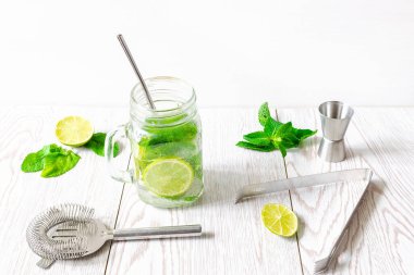 Taze buzlu mojito limonata yaz içeceği dilimlenmiş kireç, parlak yeşil nane yaprakları ve şeffaf bir fincanda donmuş buz küpleri ahşap masada taş kavanozu..