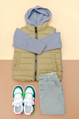 Yelek, kazak, kapüşonlu sweatshirt, örgü, spor ayakkabılı kot pantolon. Bebek kıyafetleri, kıyafetler, bahar, sonbahar, kış için aksesuarlar, kahverengi arka planda. Moda çocukları..