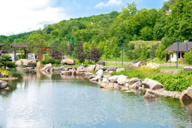 Bahçede güzel yeşil botanik manzara tasarımı, ağaçlarla, çalılarla ve banklarla dolu şehir parkı, ahşap çardak, dekoratif göl havuzu, taze çimen. Sahne yaz bahçıvanlığı arka plan, konsept