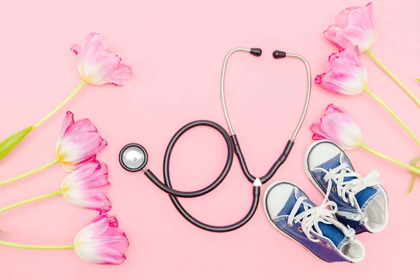 National Doctors or nurse day greeting card with stethoscope, bunch of tulips flowers,babys childs sneakers shoes on pink background.Health medicine Day.Pregnancy,motherhood, obstetrics,pediatrics.