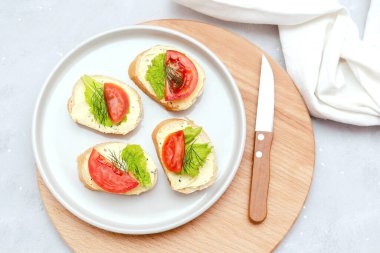 Yumuşak beyaz peynirli sandviç tostu, taze domates, ahşap kesim tahtasındaki fesleğen yeşili. Lezzetli sağlıklı vejetaryen yemekleri, İtalyan mutfağı aperatifleri. Üst görünüm düzlüğü.