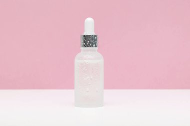 Blank white glass dropper bottle packaging with aromatic oil or serum,water drops on pink background.Natural organic Spa Cosmetic product design mockup.Front view.flat lay,copy space.