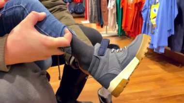 Dükkanda babasının kucağında küçük bir çocuk. Oğlu olan bir çocuk, yeni ayakkabılar giyer, seçer, yeni ayakkabılar alır. Alışveriş, çocuk kıyafetleri, moda kıyafeti, babalık, mutlu aile 4k 'si.