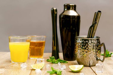 Taze buzlu limonata yaz içeceği, alkollü ya da üzümlü kokteyl, parlak yeşil nane yaprakları. Siyah karıştırıcı, bardak, ahşap masada barmen aletleri..