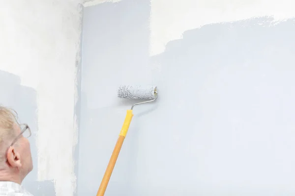 Adult senior mature man painting walls with gray brush roller,living,bedroom,moving to new apartment.male worker artist, interior decorator, repair of residential apartment.