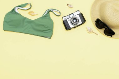 Travel vacation summer flat lay, accessories objects, hat, sunglasses, clothes, bathing suit, camera, seashells on yellow background with copy space, planning trip adventure.
