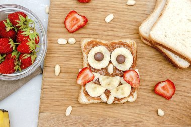 Baykuş suratlı tost ekmeği. Fıstık ezmeli, çilekli. Komik çocuklar bebekler tatlı tatlı tatlı, sağlıklı kahvaltı, öğle yemeği, ahşap tahtada yemek sanatı.