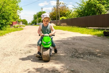 Şirin, sarışın, küçük çocuk bisiklet sürmeyi öğreniyor, çocuk motosikleti sürüyor. Fiziksel gelişim, çocuk yuvası, anaokulu kavramı, kırsal doğa manzarası..