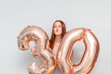 Mutlu genç ve çekici kızıl saçlı kadın 30 numaralı şenlik balonlarını tutuyor. Doğum gününü kutlamak için evde tatil partisinde gülümsüyor..