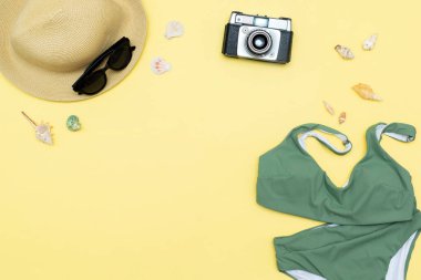 Travel vacation summer flat lay, accessories objects, hat, sunglasses, clothes, bathing suit, camera, seashells on yellow background with copy space, planning trip adventure.