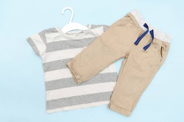 Bebek tişörtü ve kot pantolon. İlkbahar, sonbahar ya da yaz için günlük çocuk kıyafetleri ve aksesuarlar. Moda çocuk kıyafeti, mavi arka planda giysiler. Düz yatıyordu, üstten, yukarıdan..