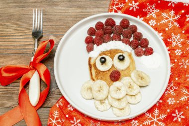 Noel Baba çocuklara kahvaltı için taze ahududu muzlu krep yaptı. Ahşap arka planda yeni yıl süslemeleri olan xmas yemekleri