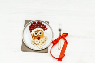 Noel Baba çocuklara kahvaltı için taze ahududu muzlu krep yaptı. Beyaz ahşap arka planda yeni yıl süslemeleri olan xmas yemekleri.