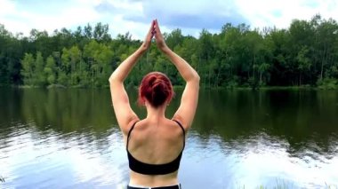 İnce tefek bir genç kızın meditasyon yapması, yoga yapması, ellerini göl, nehir, su, zihin temizleme gevşetici yakınına kaldırması..