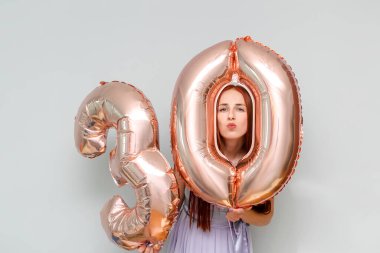 Mutlu genç ve çekici kızıl saçlı kadın 30 numaralı şenlik balonlarını tutuyor. Doğum gününü kutlamak için evde tatil partisinde gülümsüyor..