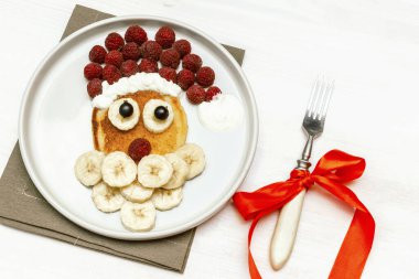 Noel Baba çocuklara kahvaltı için taze ahududu muzlu krep yaptı. Beyaz ahşap arka planda yeni yıl süslemeleri olan xmas yemekleri