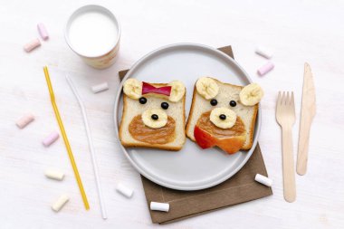 Komik sevimli ayı, köpek suratlı tost ekmeği fıstık ezmeli, muzlu, elmalı, sütlü, şekerli. Çocuklar bebeğin tatlı, sağlıklı kahvaltı tabağında öğle yemeği sanatı, yakın plan, üst manzara.