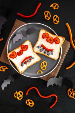 Cadılar bayramında kızarmış ekmek, tereyağı, çilek, şeker, servis tahtası, siyah arka planda yarasalar. Çocuklar tatlı tatlı tatlı kahvaltı öğle yemeği.