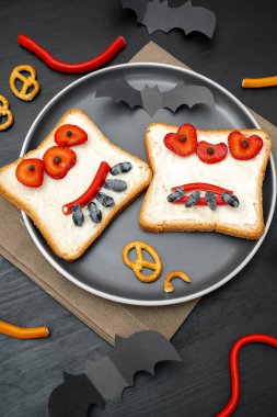 Cadılar bayramında kızarmış ekmek, tereyağı, çilek, şeker, servis tahtası, siyah arka planda yarasalar. Çocuklar tatlı tatlı tatlı kahvaltı öğle yemeği.