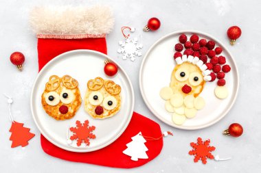 Christmas Santa Claus,deers face shaped pancake with fresh raspberry berry,cheese on plate for kids baby children breakfast dinner. xmas food with new year decorations on gray background copy space.
