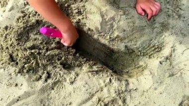 Yaz tatilinde kumsalda kumla oynayan küçük çocuk elleri, oyuncak plastik kürekle kum havuzunda çukur kazıyor. Çocuk deniz kenarında kumdan kale inşa ediyor.