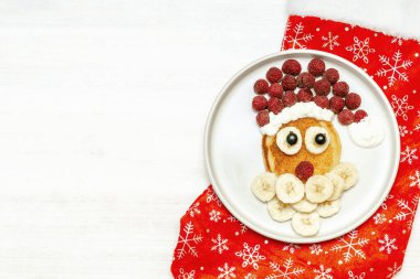 Noel Baba, tatlı taze ahududu ve muzlu krep şeklinde tabakta kırmızı çorap beyaz tahta arka planda çocuklar için kahvaltı. Yeni yıl süslemeleri ile xmas yemekleri.