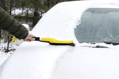 Adam arabanın ön camından fırçayla kar ve buz fırçalıyor. Kışın arabadan kar fırtınası üstüne taze kar temizleyen kişi. Ön camda kar tabakası, pencere. Araç aşırı hava koşullarında.