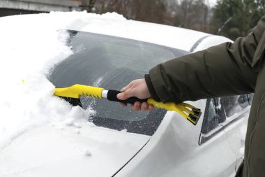 Adam arabanın ön camından fırçayla kar ve buz fırçalıyor. Kışın arabadan kar fırtınası üstüne taze kar temizleyen kişi. Ön camda kar tabakası, pencere. Araç aşırı hava koşullarında.