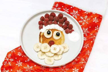 Noel Baba gözlemesi, ahududu, muz, çocuk kahvaltısı için beyaz arka planda kırmızı çorap. Yeni yıl süslemeleri ile xmas yemekleri.