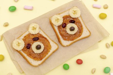 Komik şirin ayı suratlı sandviç ekmeği fıstık ezmeli, muzlu, fındıklı, lokumlu. Çocuklar bebekler tatlı tatlı tatlı sağlıklı kahvaltı tabakta yemek sanatı, yakın plan, üst manzara.