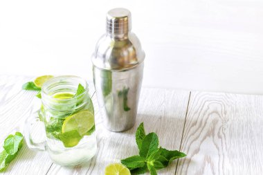 Taze buzlu mojito limonata yaz içeceği dilimlenmiş limonlu kokteyl, parlak yeşil nane yaprakları şeffaf bir fincanda titretici ve donmuş buz küpleri ahşap masada taş kavanozu..