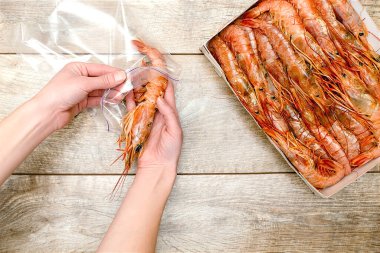 Kadın çiğ karidesleri, karidesleri kutudan plastik dondurucuya koyuyor, ahşap arka planda fotokopi alanı olan..