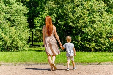 Anne ve çocuk çocuk çocuk parkta yürüyorlar. Mutlu aile oyunları, el ele tutuşmalar, ebeveynlik, çocuk bakımı. Dışarıda sağlıklı bebek zamanı anneliği, doğa..