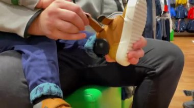 Oğlu olan baba giyer, seçer, ayakkabı seçer, yeni ayakkabılar alır. Babasının kucağındaki küçük çocuk, alışveriş, çocuk kıyafetleri, moda kıyafeti, babalık, mutlu aile 4k 'si.