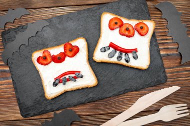 Cadılar bayramında kızarmış ekmek, tereyağı, çilek, şeker, servis masası, siyah arka planda yarasalar. Çocuklar için tatlı öğle yemeği..